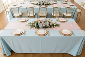rectangular table features a light blue tablecloth, a soft pink runner, and a centerpiece of pink roses and blue hydrangeas