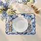 Two blue French Toile placemats with scalloped edges under a white plate and gold flatware, on a beige table with flowers.