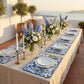 Blue French toile scalloped-edge placemats (set of two) on an outdoor table with white plates, candlesticks, and florals.