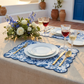 Blue French toile scalloped-edge placemats set on a beige tablecloth with white plates, gold flatware, and floral centerpiece