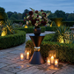 31" Tall Hourglass Plinth Pedestal Stand Black outside with vase of mixed floral and candles in a garden