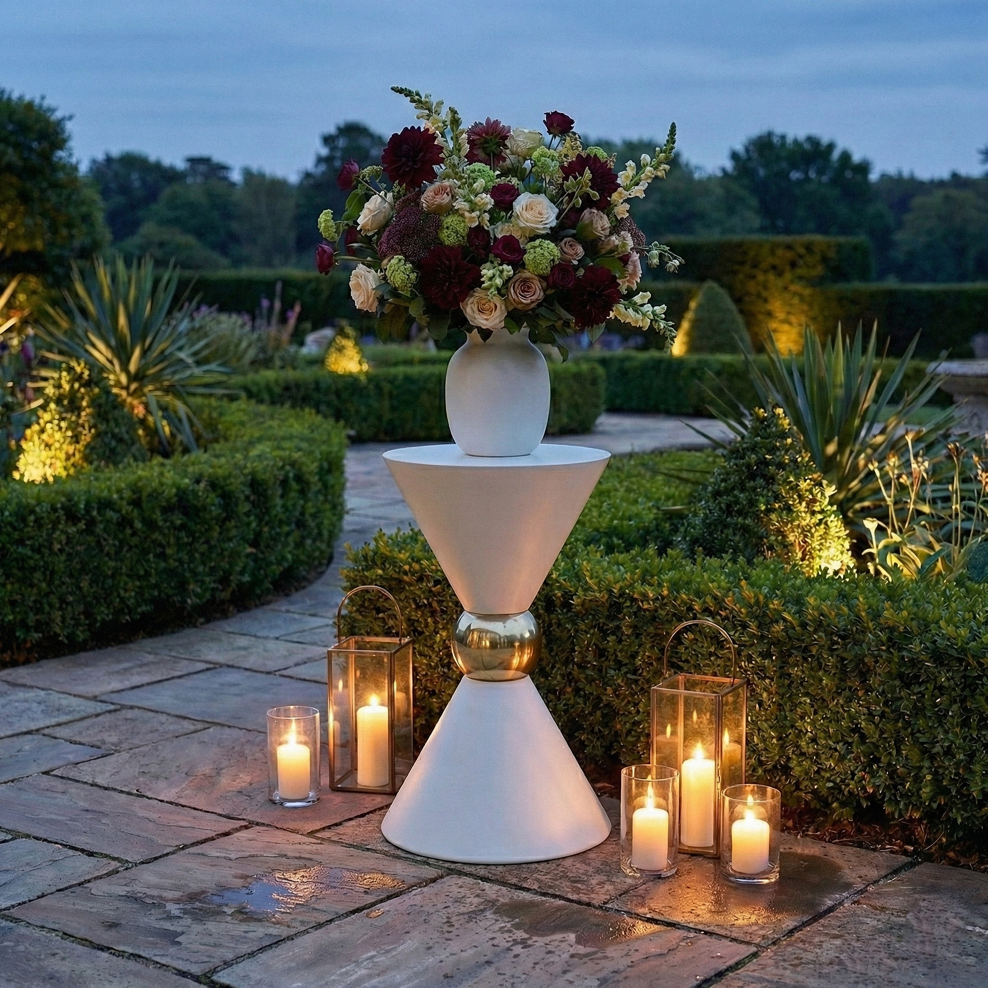 35" Tall Hourglass Plinth Pedestal Stand White outdoor garden set up with gold pillar candles, and a vase of mixed florals