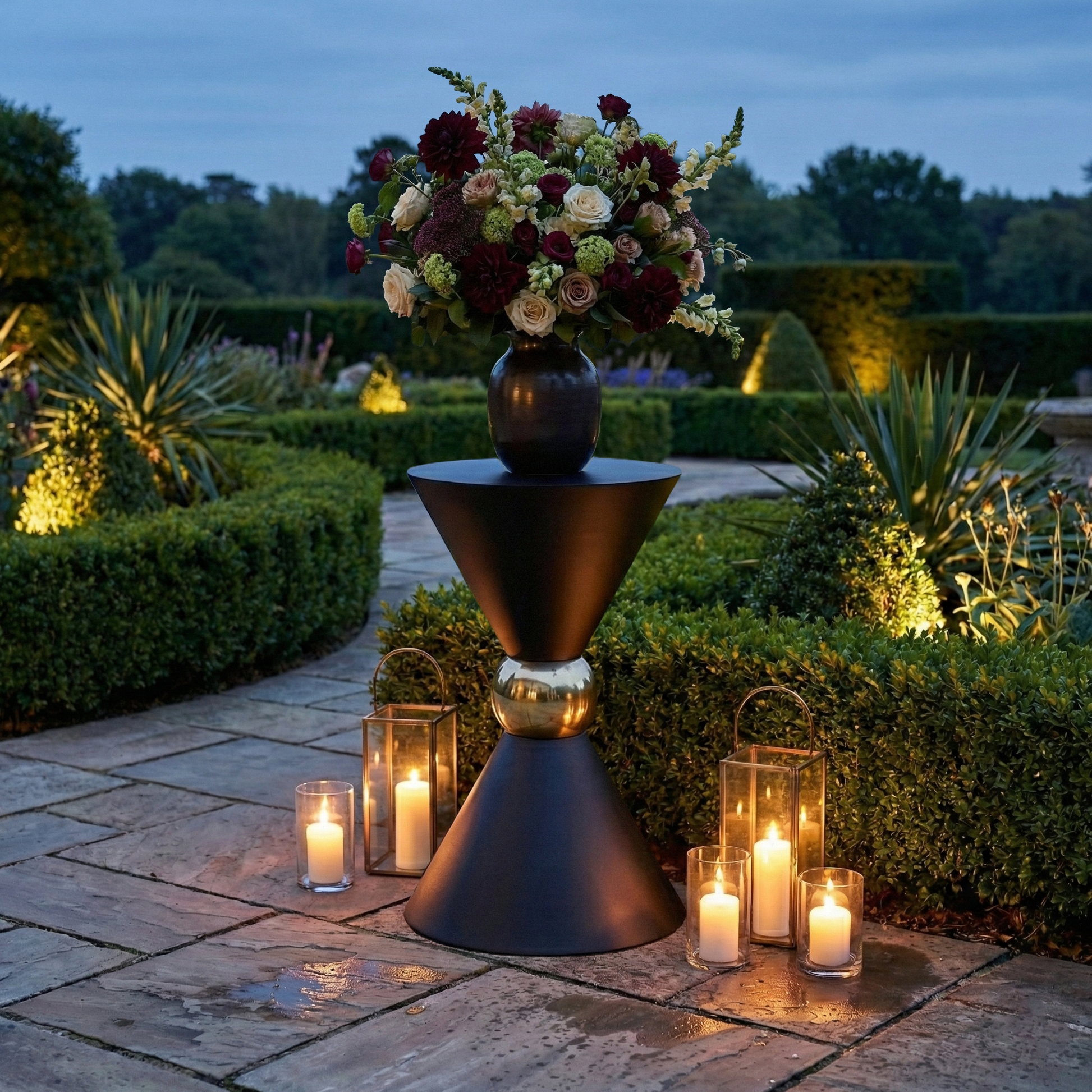 38" Tall Hourglass Plinth Pedestal Stand Black outside with vase of mixed floral and candles in a garden