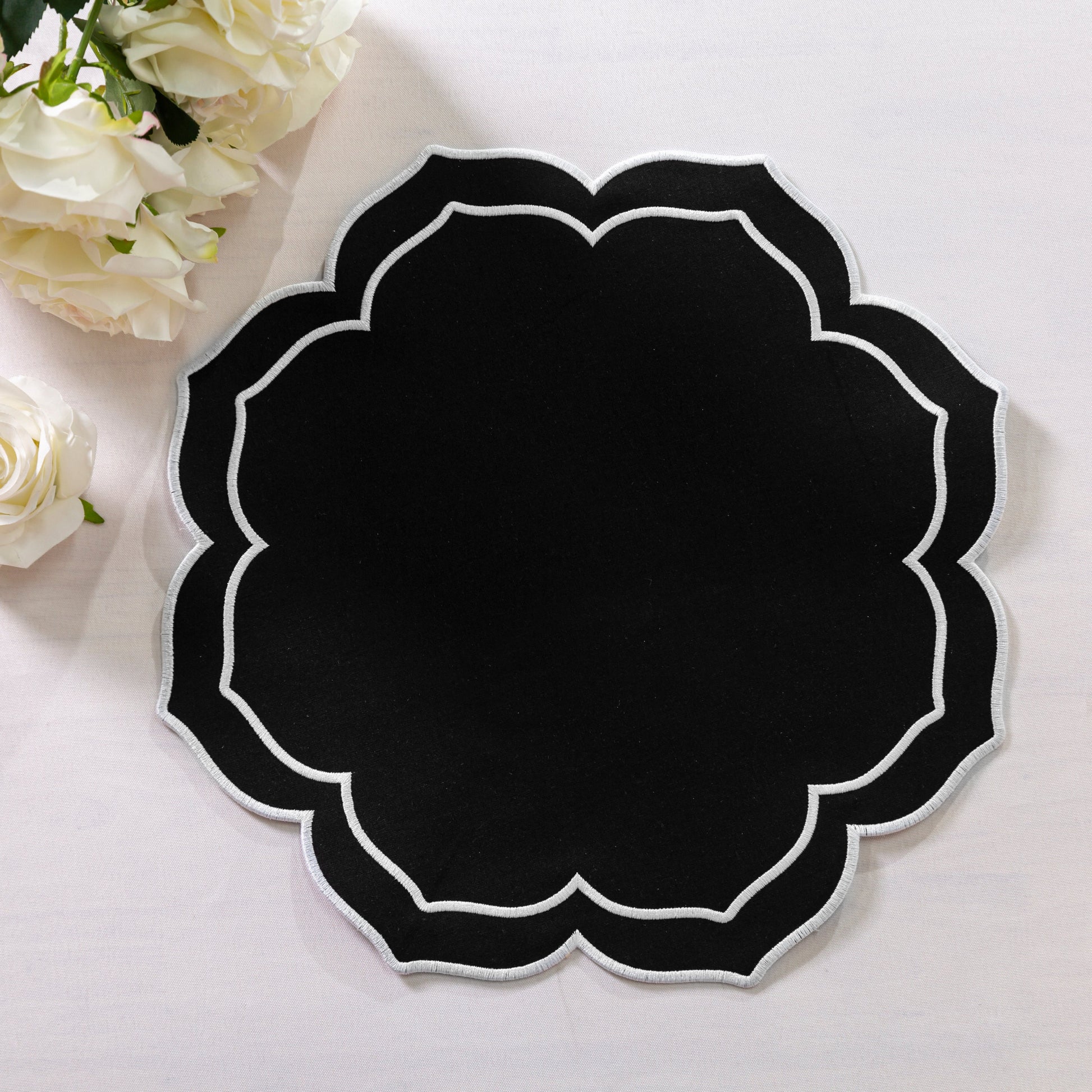 4pc/set Petal Elegance Placemats - Black/White Trim paired with a white tablecloth, and white roses