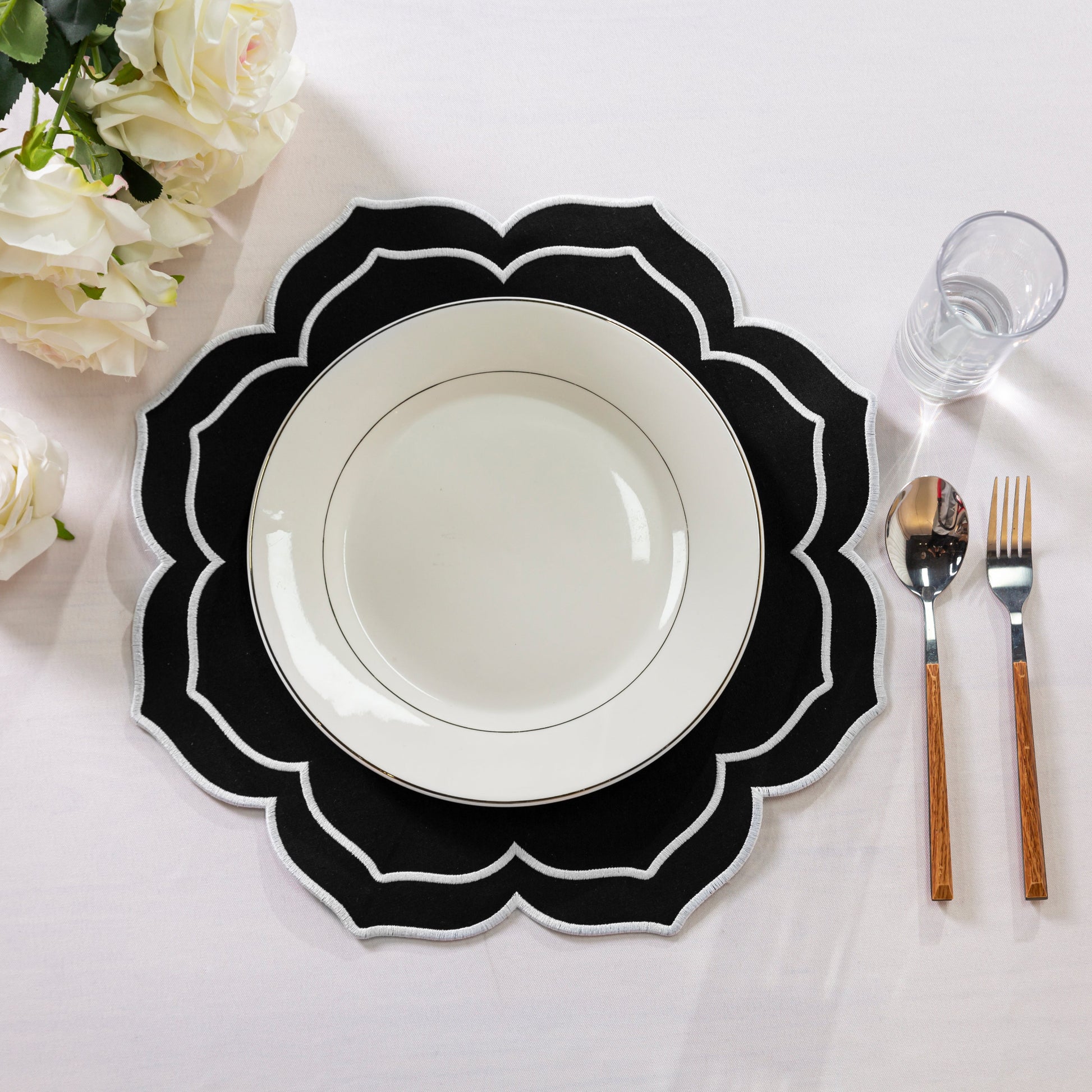 4pc/set Petal Elegance Placemats - Black/White Trim paired with a white tablecloth, white dinner plate, white roses and silverware