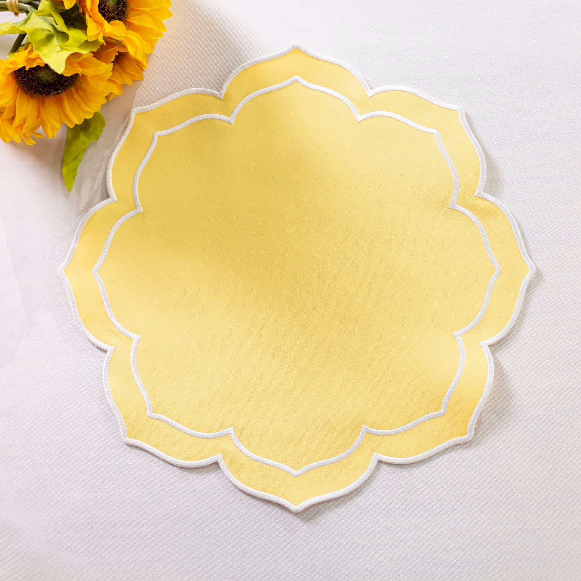 Petal Elegance Placemats - Pastel Yellow/White Trim on top of a white tablecloth and sunflowers
