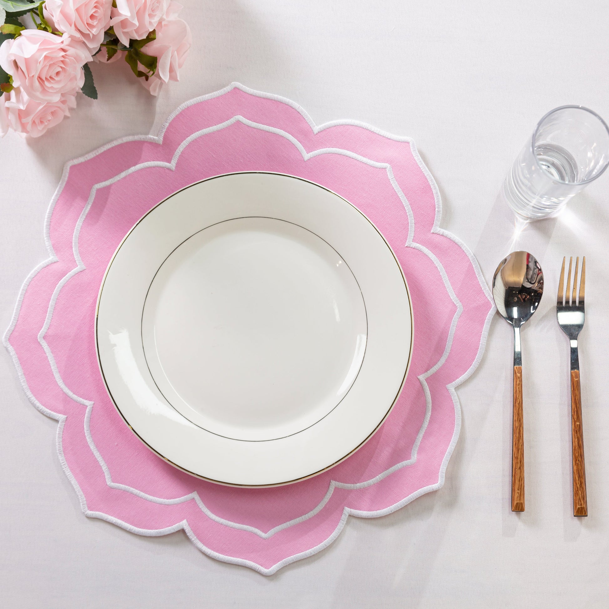4pc/set Petal Elegance Placemats - Pink/White Trim on top an ivory tablecloth, pink roses, white dinner plate and silverware