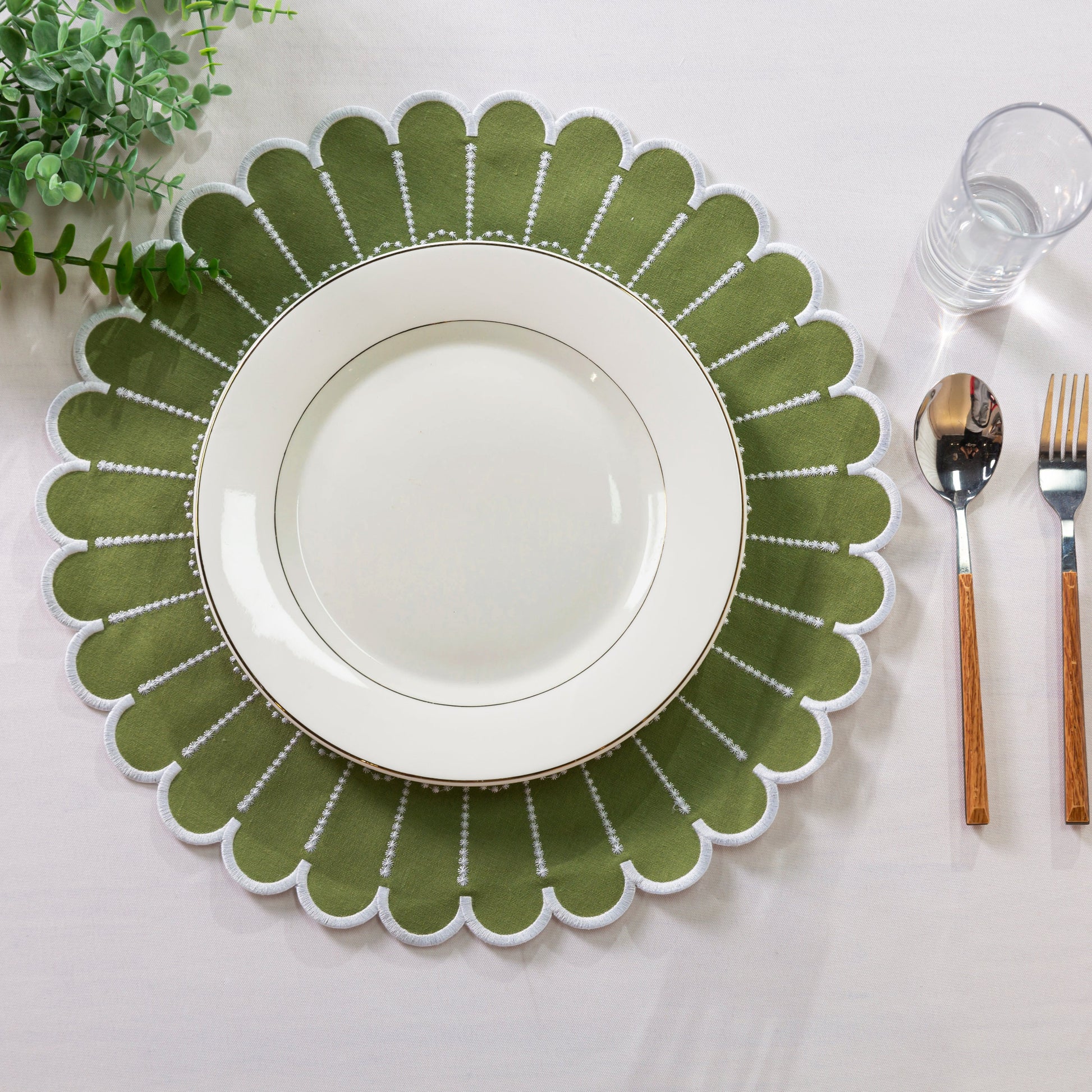 4pc/set Sunburst Edge Placemats Olive Green/White Trim paired with white dinner plate, faux greenery, silverware on a white tablecloth