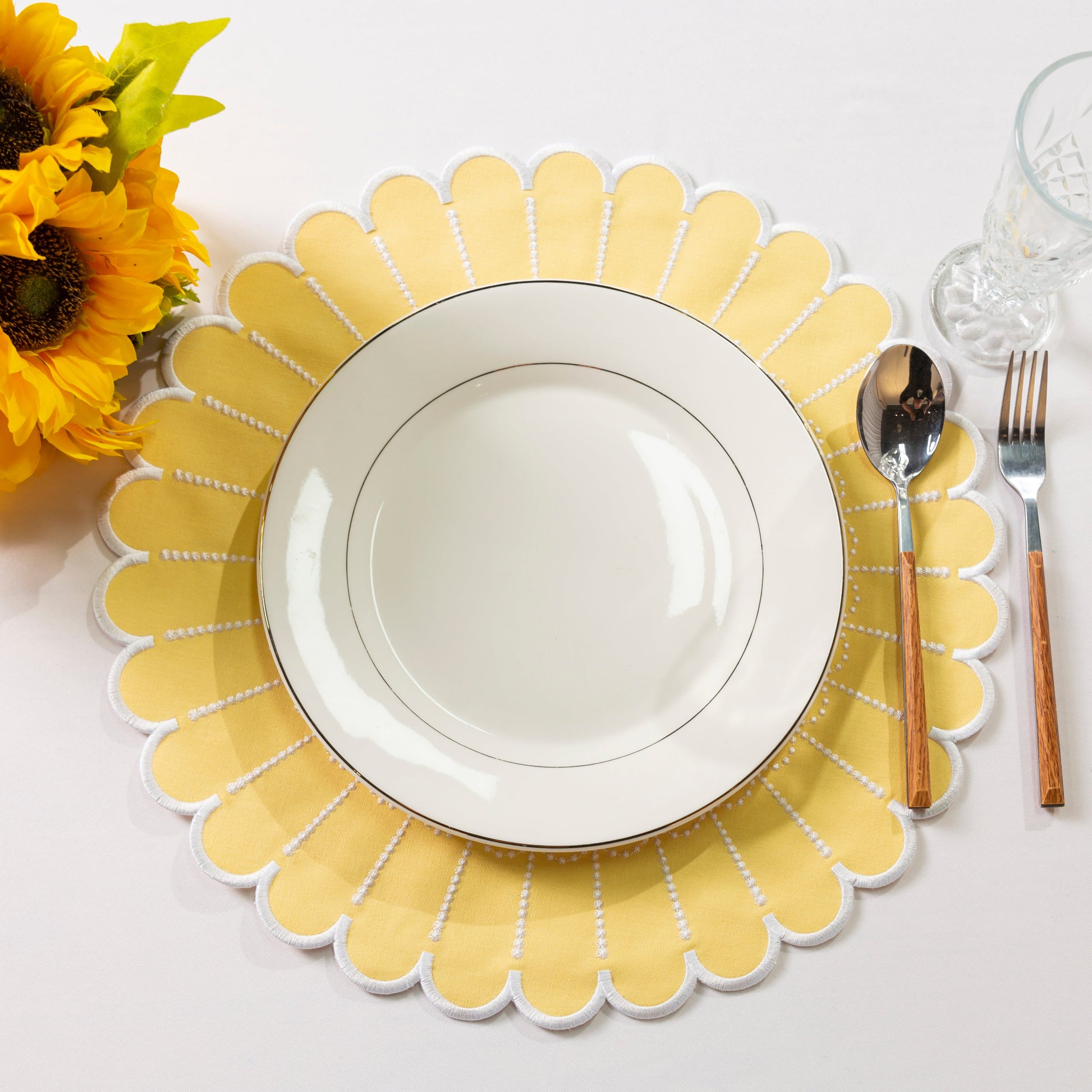 4pc/set Sunburst Edge Placemats Pastel Yellow/White Trim paired with white dinner plate, florals, silverware on a white tablecloth