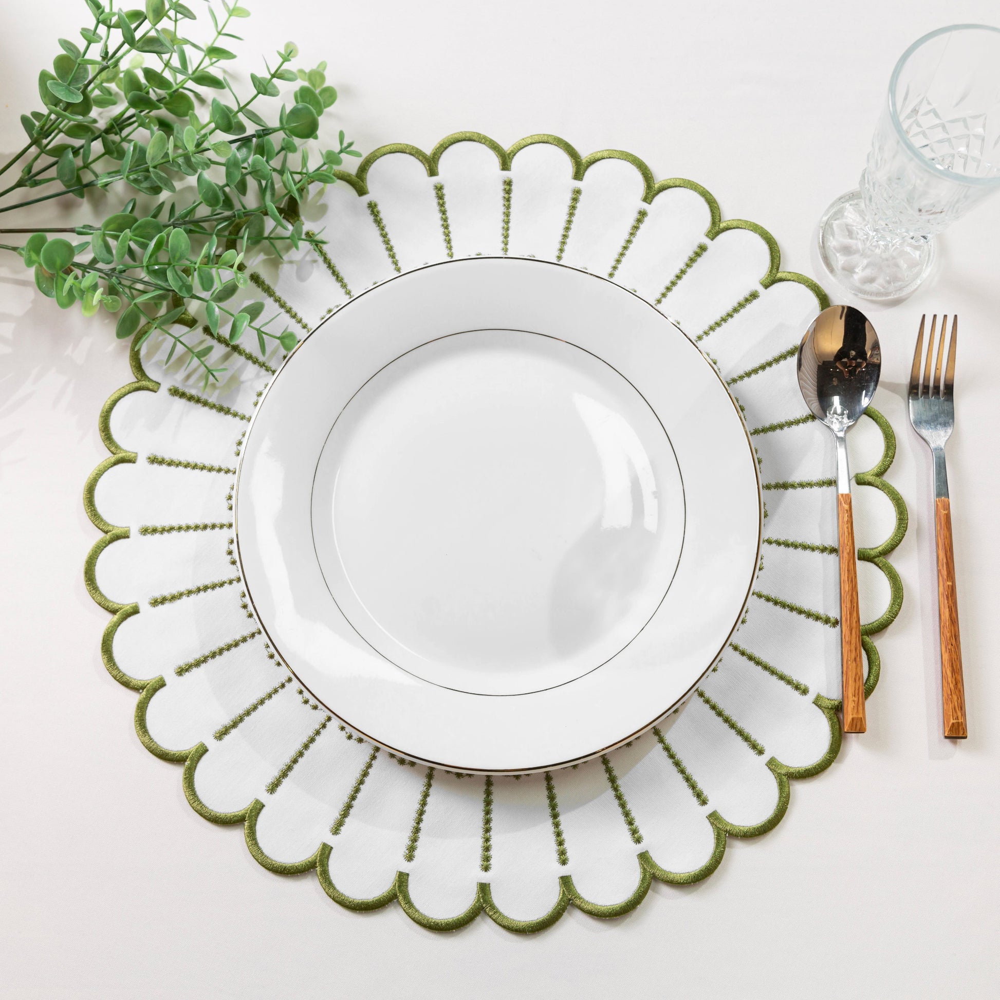 4pc/set Sunburst Edge Placemats White/Olive Green Trim paired with a white dinner plate, faux greenery, silverware on a white tablecloth