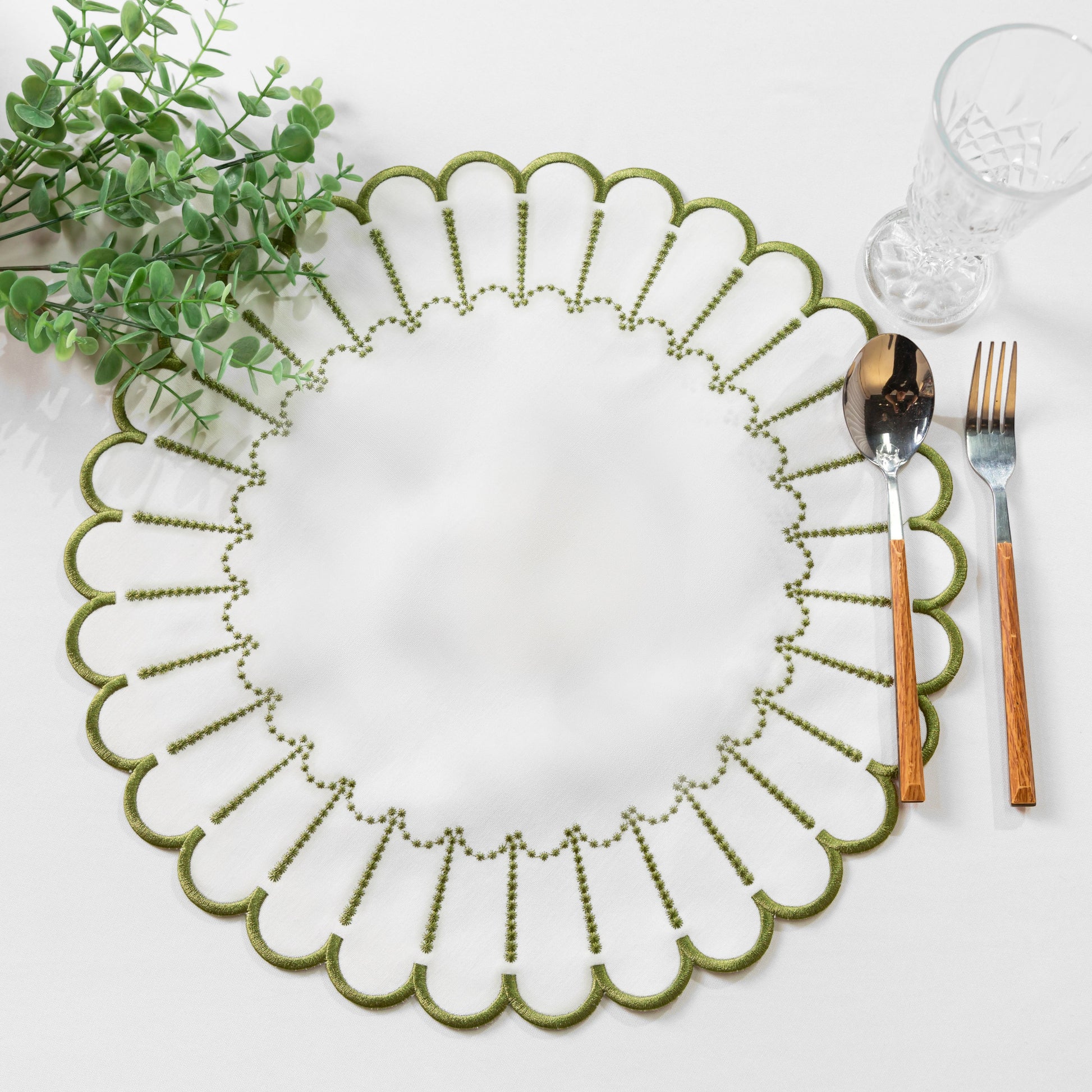 4pc/set Sunburst Edge Placemats White/Olive Green Trim paired with faux greenery, silverware on a white tablecloth
