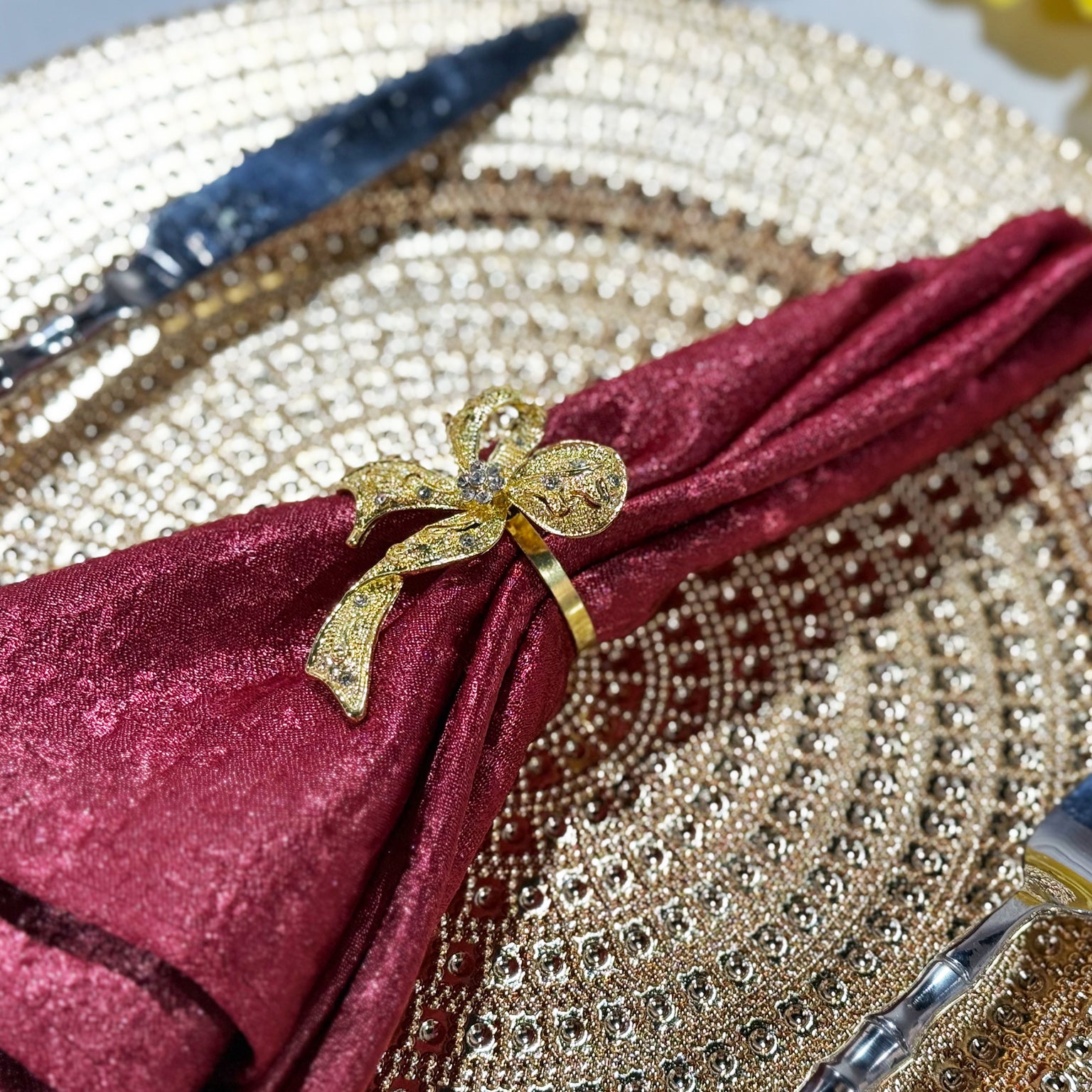 Crinkle Shimmer Napkin 20"x20" - Burgundy folded with a gold bow napkin ring close up