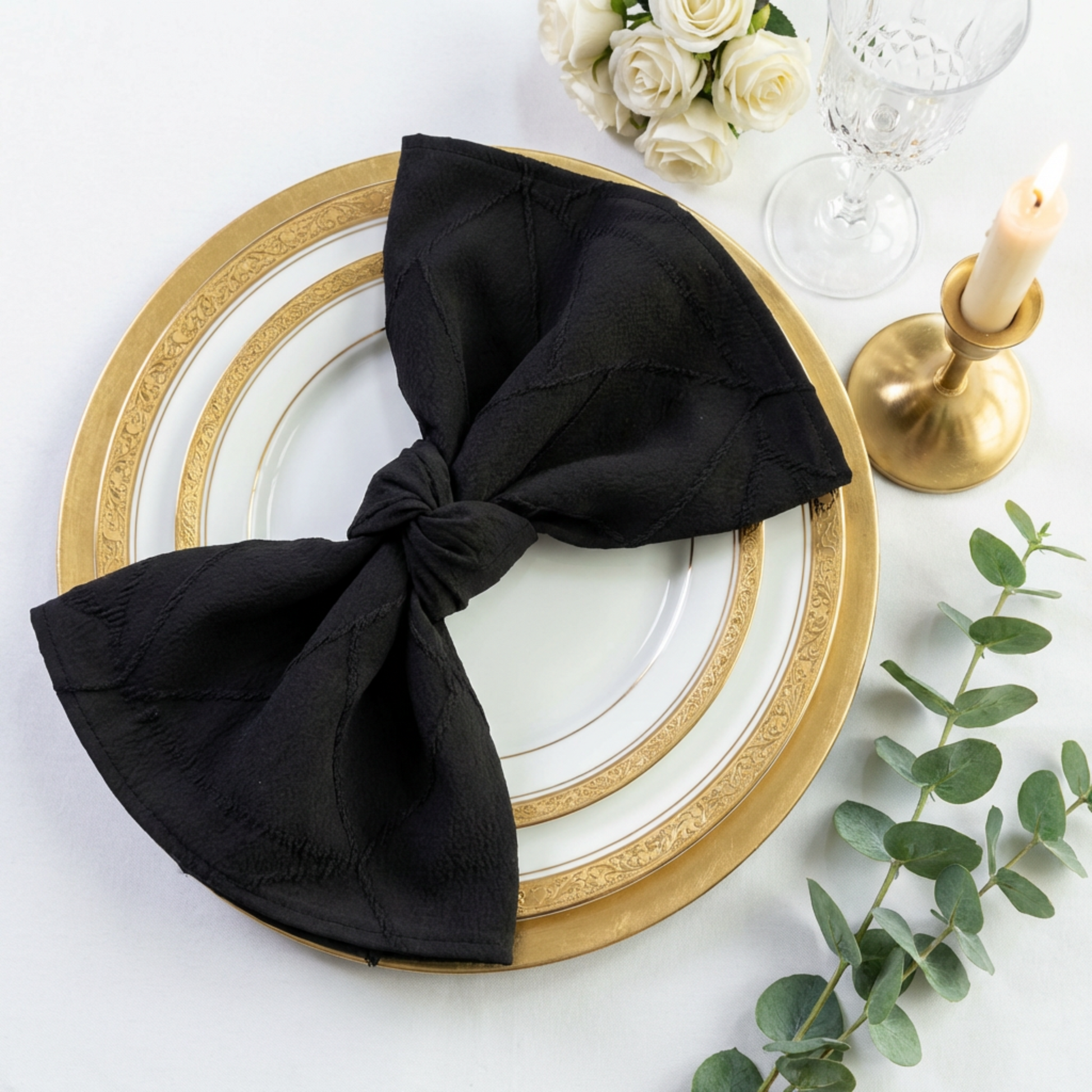 Embossed Geometric Jacquard Napkin 20"x20" Black folded in a shape of a bow-tie on top of white/gold dinner plates