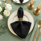 Embossed Geometric Jacquard Napkin 20"x20" Black paired with a gold napkin ring, on top a dinner plate and sage green tablecloth