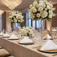 Embossed Geometric Jacquard Napkin 20"x20" White on top of gold charger plates, tall white floral centerpieces and floating candles