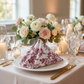 close up of the French Toile 20"x20" Linen Napkin Burgudy in a triangle fold on a white dinner plate