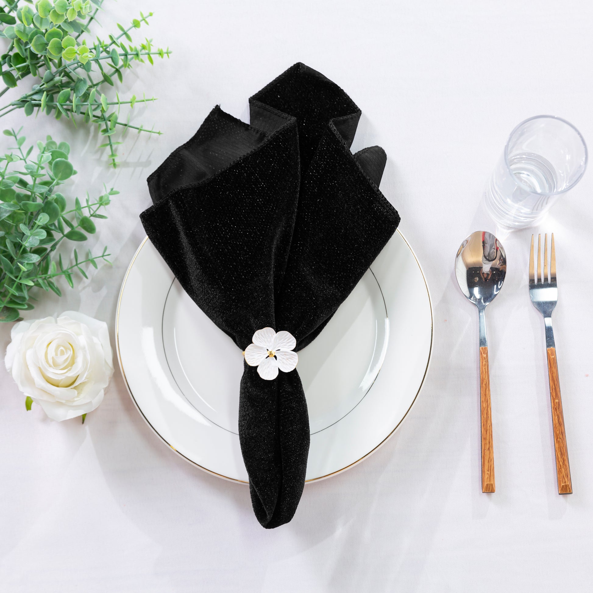 5 pcs/pk Glitter Velvet 20"x20" Linen Napkin Black on a white charger plate with a white flower napkin ring, and silverware