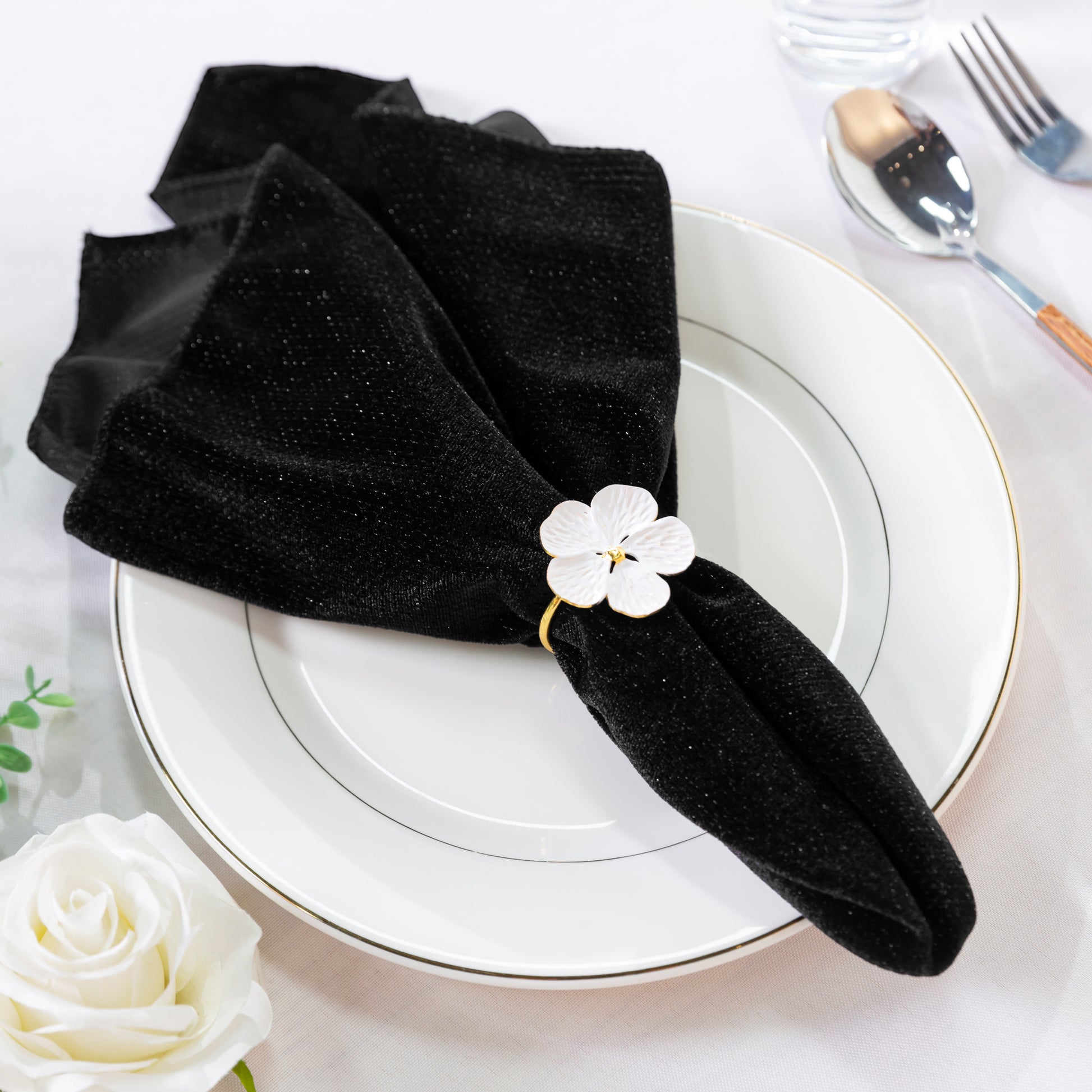 5 pcs/pk Glitter Velvet 20"x20" Linen Napkin Black on a white charger plate with a white flower napkin ring