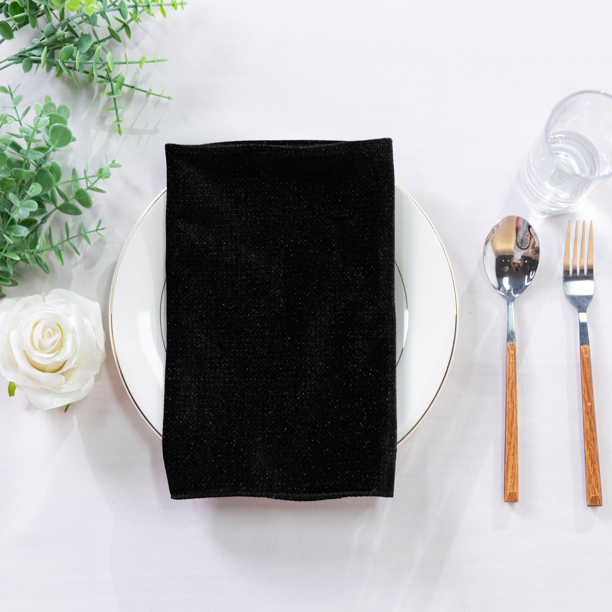 5 pcs/pk Glitter Velvet 20"x20" Linen Napkin Black on a white charger plate with greenery and white rose