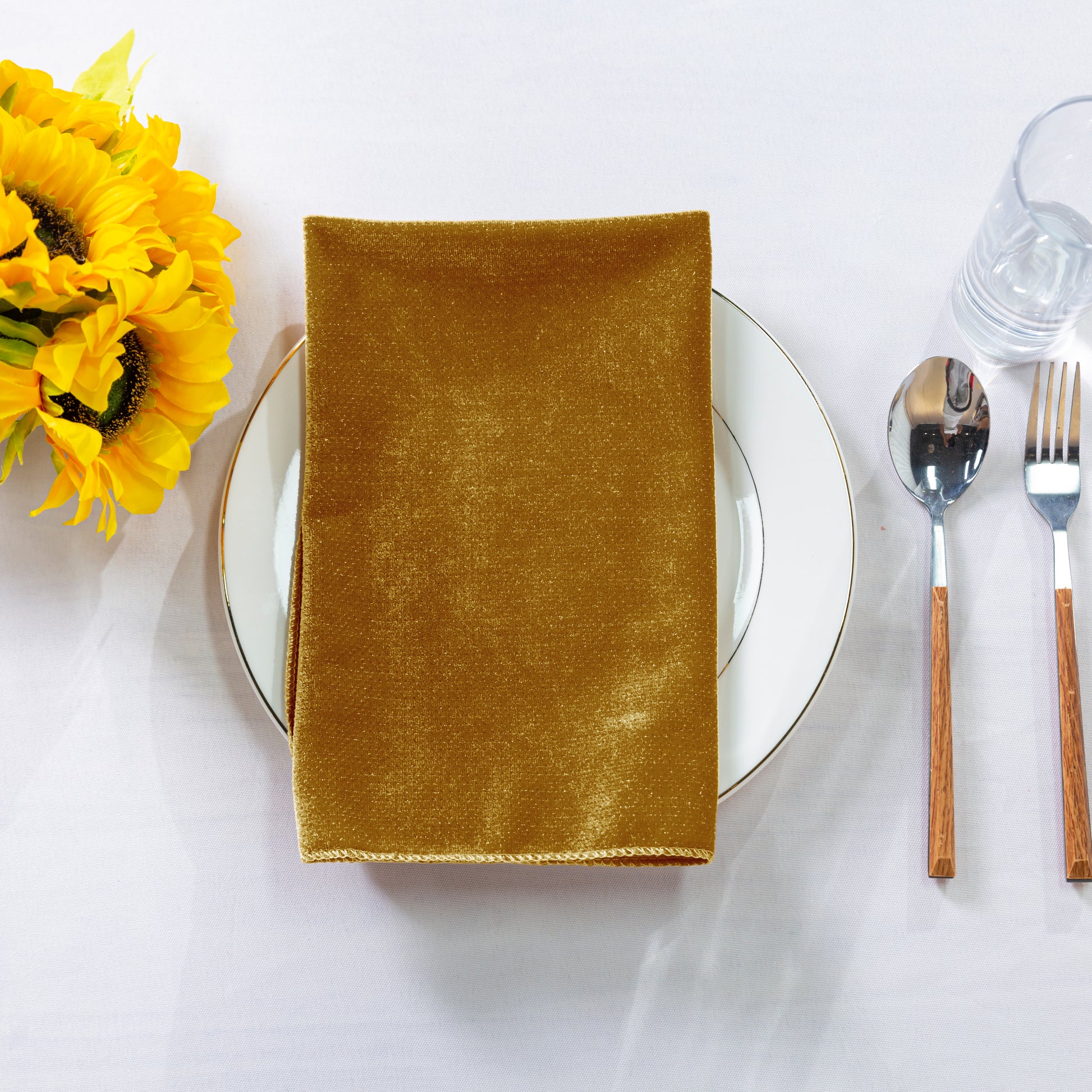 5 pcs/pk Glitter Velvet 20"x20" Linen Napkin Gold folded on a white charger plate, sunflowers and silverware