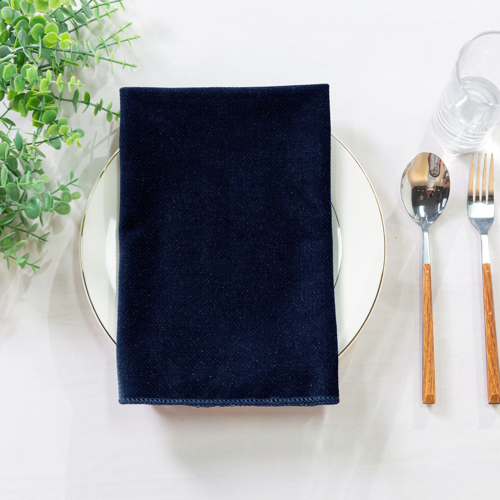 5 pcs/pk Glitter Velvet 20"x20" Linen Napkin folded on a white charger plate, greenery and silverware
