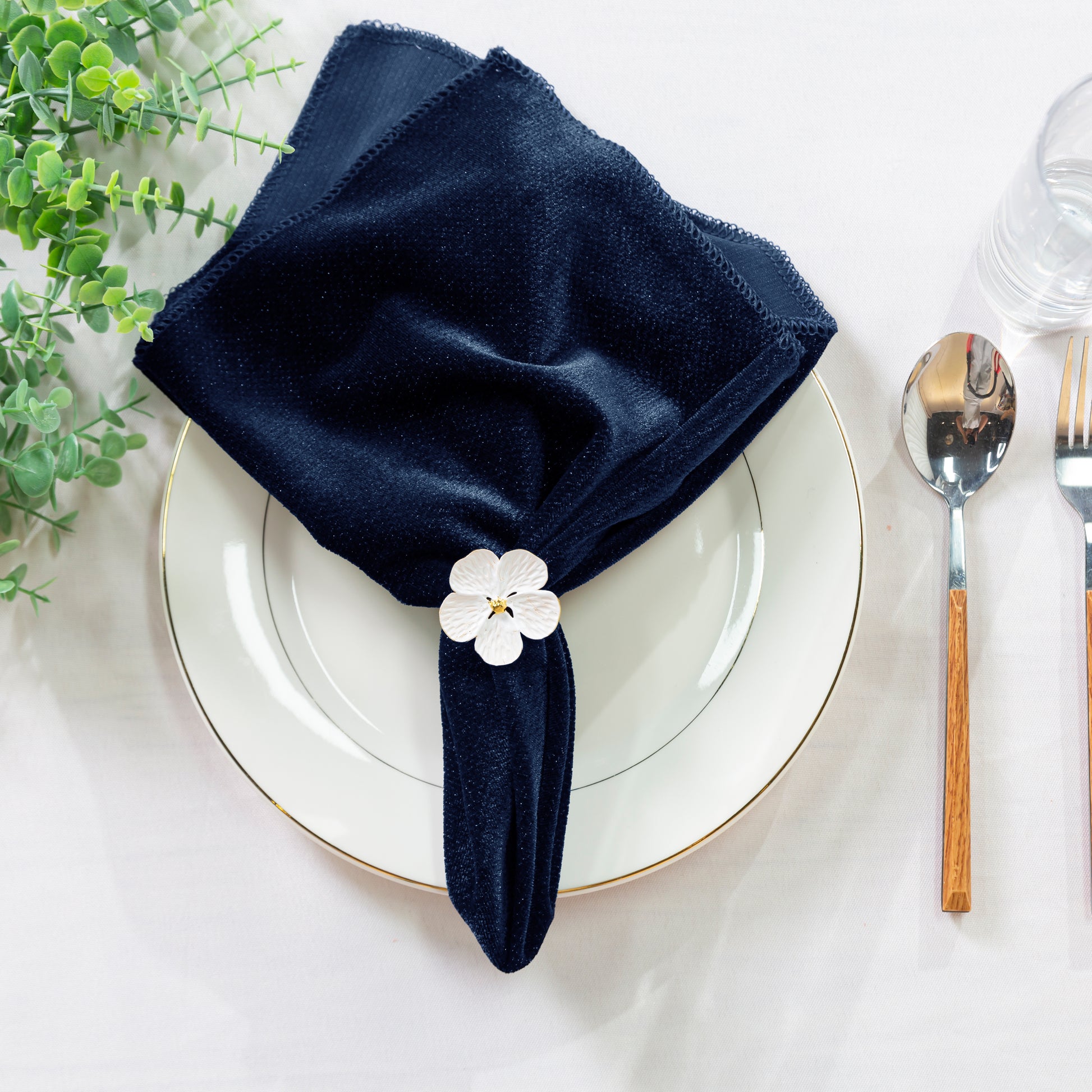 5 pcs/pk Glitter Velvet 20"x20" Linen Napkin Navy Blue paired with a flower napkin ring, white charger plate, faux greens and silverware
