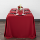 front view showing 90"x132" Rectangular Oblong Premium Polyester Tablecloth - Apple Red with silver charger plate and apple red napkin
