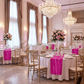 wedding tables with the Accordion Crinkle Taffeta Table Runner Fuchsia on top a white tablecloth, wine glasses, and tall floral centerpieces