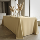 An informal dinner table setting with the Scuba King 108"x156" Rectangular Tablecloth Champagne paired with different shaped white vases with champagne pampas stems