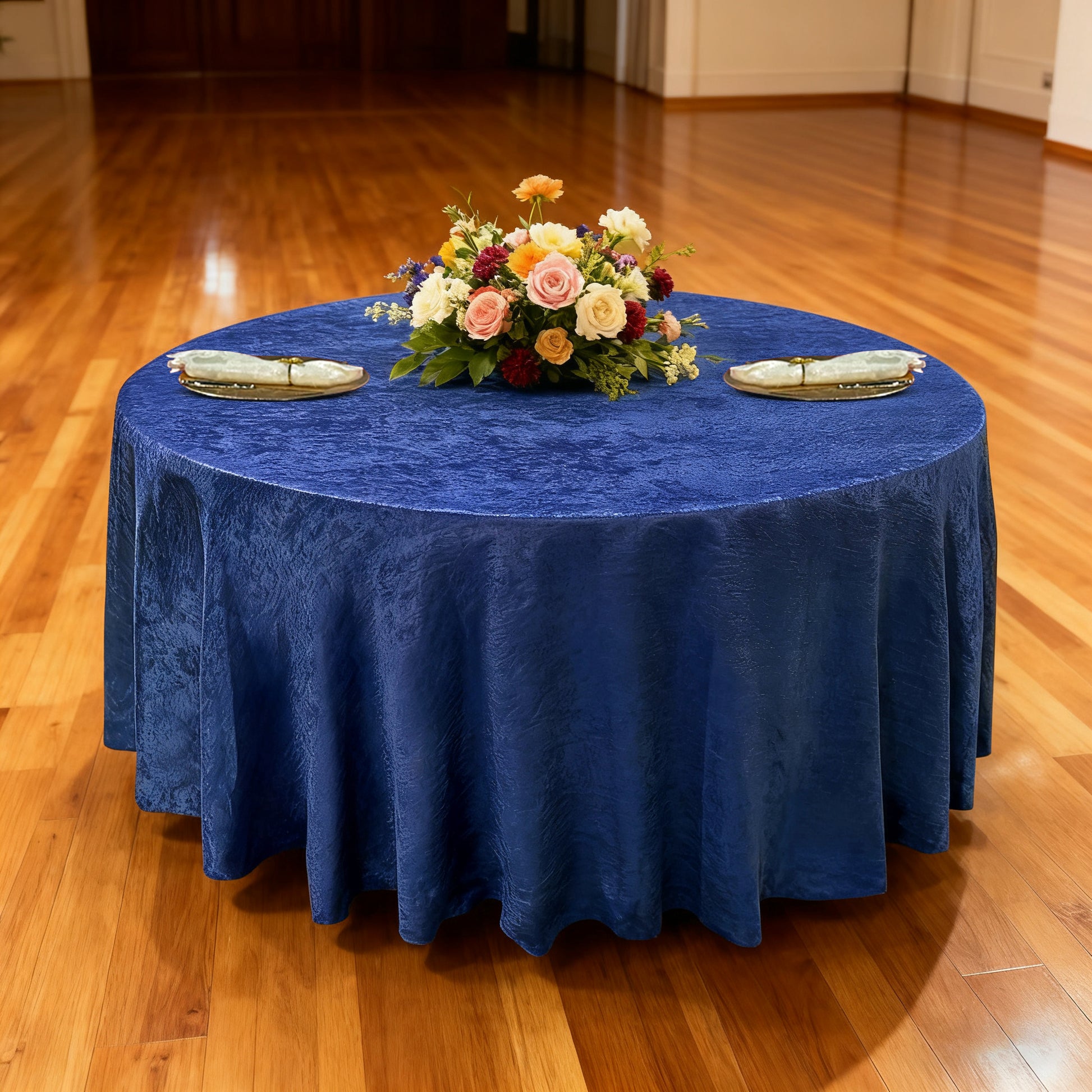 Crinkle Shimmer 132" Round Tablecloth Royal Blue with gold charger plates, ivory napkins, and a floral centerpiece