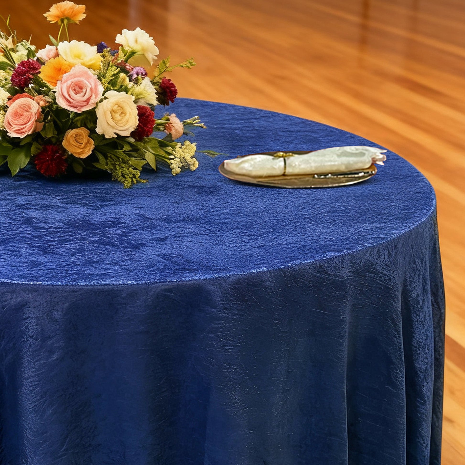 Crinkle Shimmer 132" Round Tablecloth Royal Blue with a floral centerpiece, gold charger plate and ivory napkin with a gold napkin ring