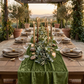 outdoor gathering with the Velvet Table Runner Dark Sage Green on a natural wood table, luxury boucle beige napkin with gold napkin rings, eucalyptus table runner and tapered candles