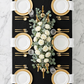 overview of the Embossed Geometric Jacquard 90"x156" Rectangle Tablecloth Black with gold charger plates, white dinner plates, gold silverware and floral centerpiece