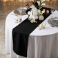 Embossed Geometric Jacquard Table Runner Black on top a round white tablecloth paired with silver charger plates, white and black flrals, silver tea light candle holders