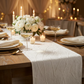 minimalist table setting with the Embossed Geometric Jacquard Table Runner Light Ivory/Off White on top a brown table, gold charger plates, white floral centerpiece and tapered candles