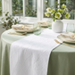 Embossed Geometric Jacquard Table Runner White on top a sage green tablecloth, with beige napkins, gold napkin rings and water glasses