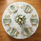 birds eye view table mockup with the French Toile 132" Round Tablecloth Sage Green, napkins sage green, white roses centerpiece and wine goblets