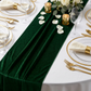 Glitter Velvet Table Runner Emerald Green close up on a white round tablecloth, with white gold trimmed charger plates
