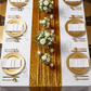 birdseye view of the Glitter Velvet Table Runner Gold on a rectangular table setting with beaded gold charger plates and white floral centerpieces
