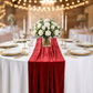 Glitter Velvet Table Runner Red on top a white tablecloth paired with gold charger plates, tapered candles, wine goblets and white roses floral centerpiece