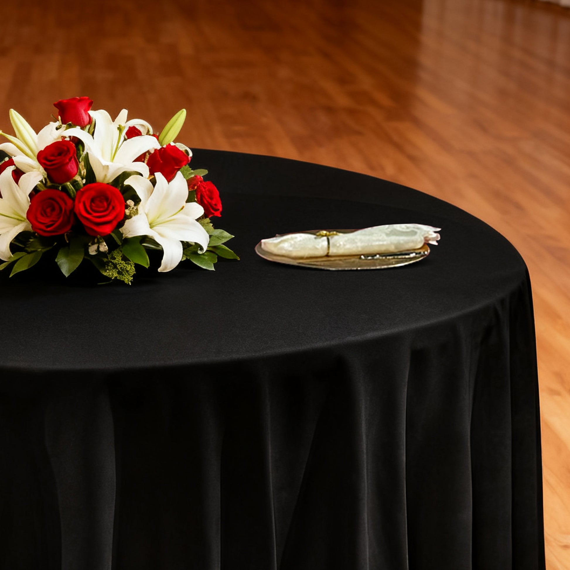 Premium 120" Round Black Spun Polyester Tablecloth with gold chargers, ivory napkins and floral centerpiece
