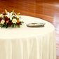 Premium 120" Round Ivory Spun Polyester Tablecloth table setting with floral centerpiece, gold charger plate and ivory napkin