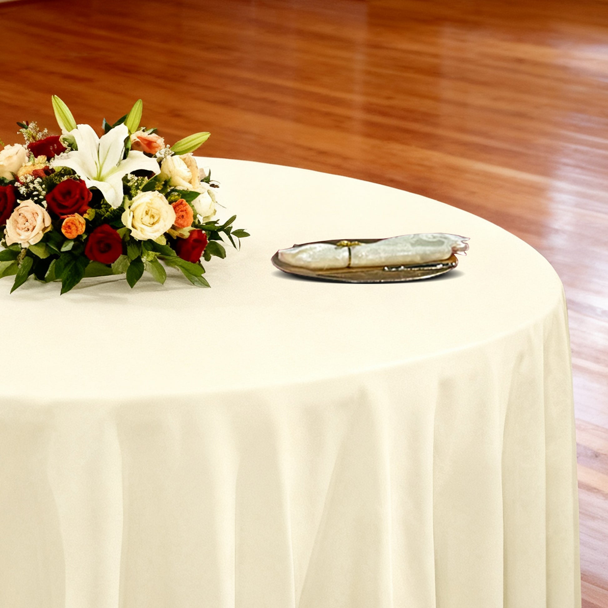 Premium 132" Round Ivory Spun Polyester Tablecloth table setting with floral centerpiece, gold charger plate and ivory napkin