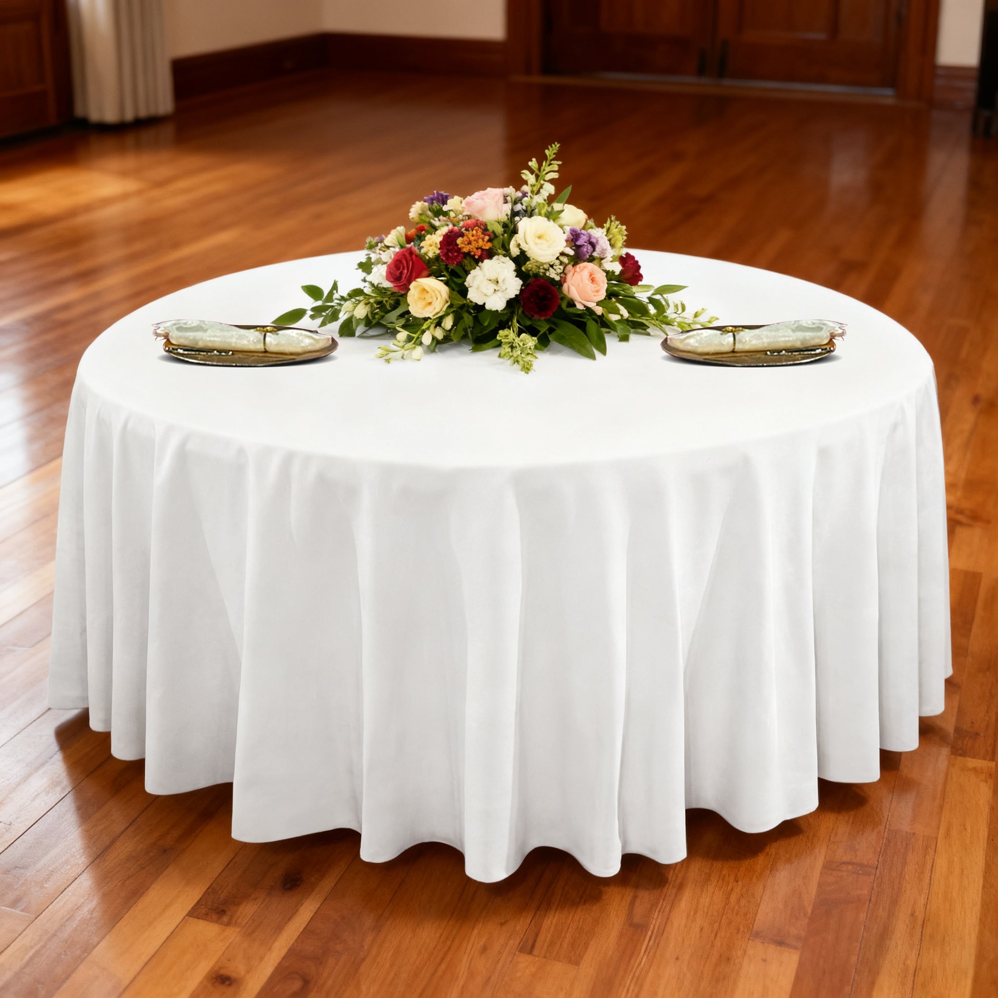 Premium 132" Round White Spun Polyester Tablecloth table setting with floral centerpiece, ivory napkins and gold charger plates