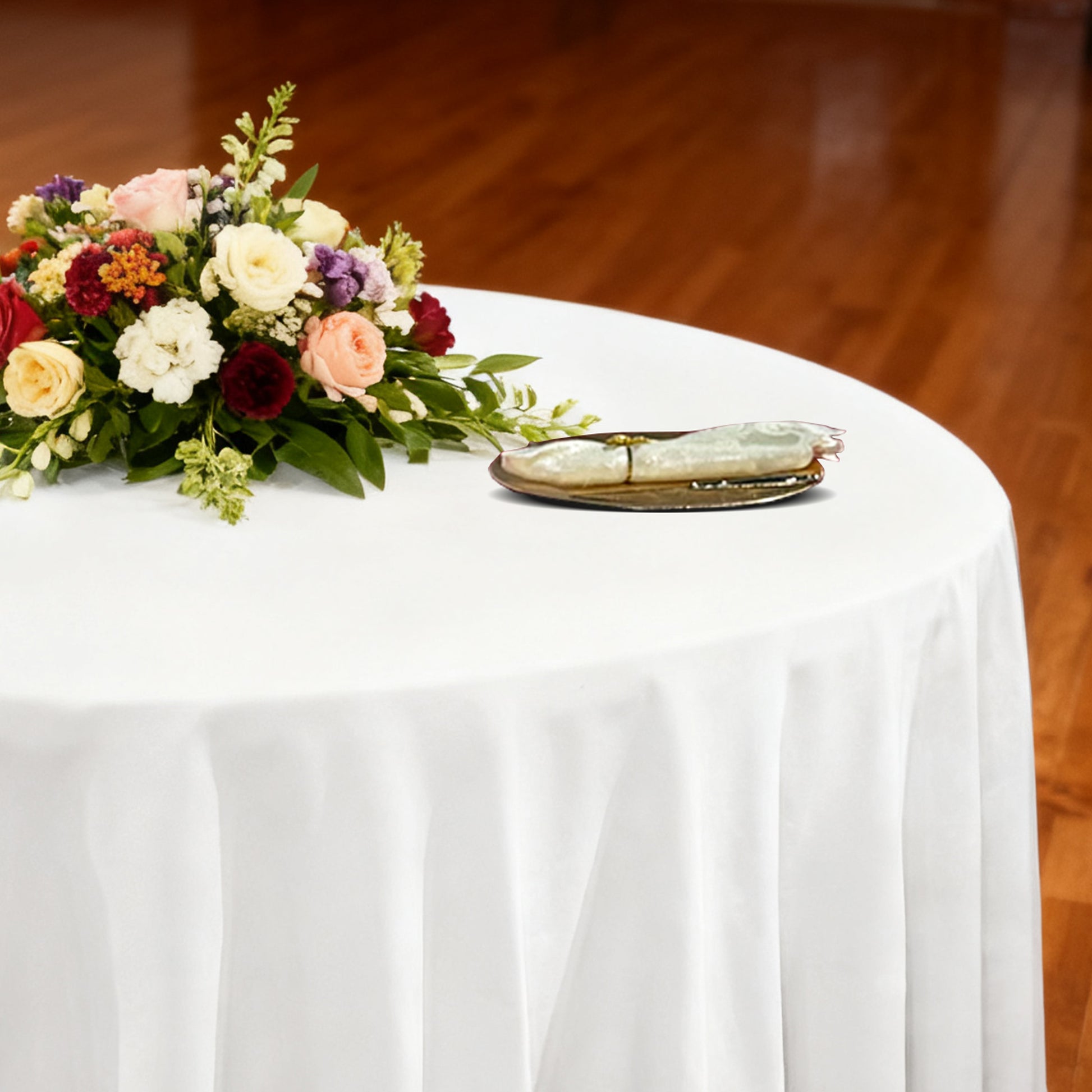 Premium 132" Round White Spun Polyester Tablecloth table setting with floral centerpiece, ivory napkin and gold charger plate