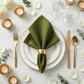 Polyester Napkin olive green with a gold napkin ring on top a white gold trimmmed dinner olates with gold flatware