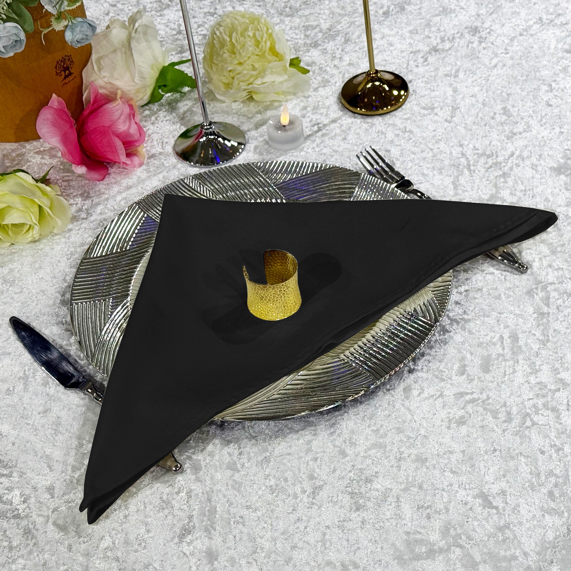 Premium Spun Polyester Napkin 20"x20" Black ontop a silver charger plate with a gold napkin ring