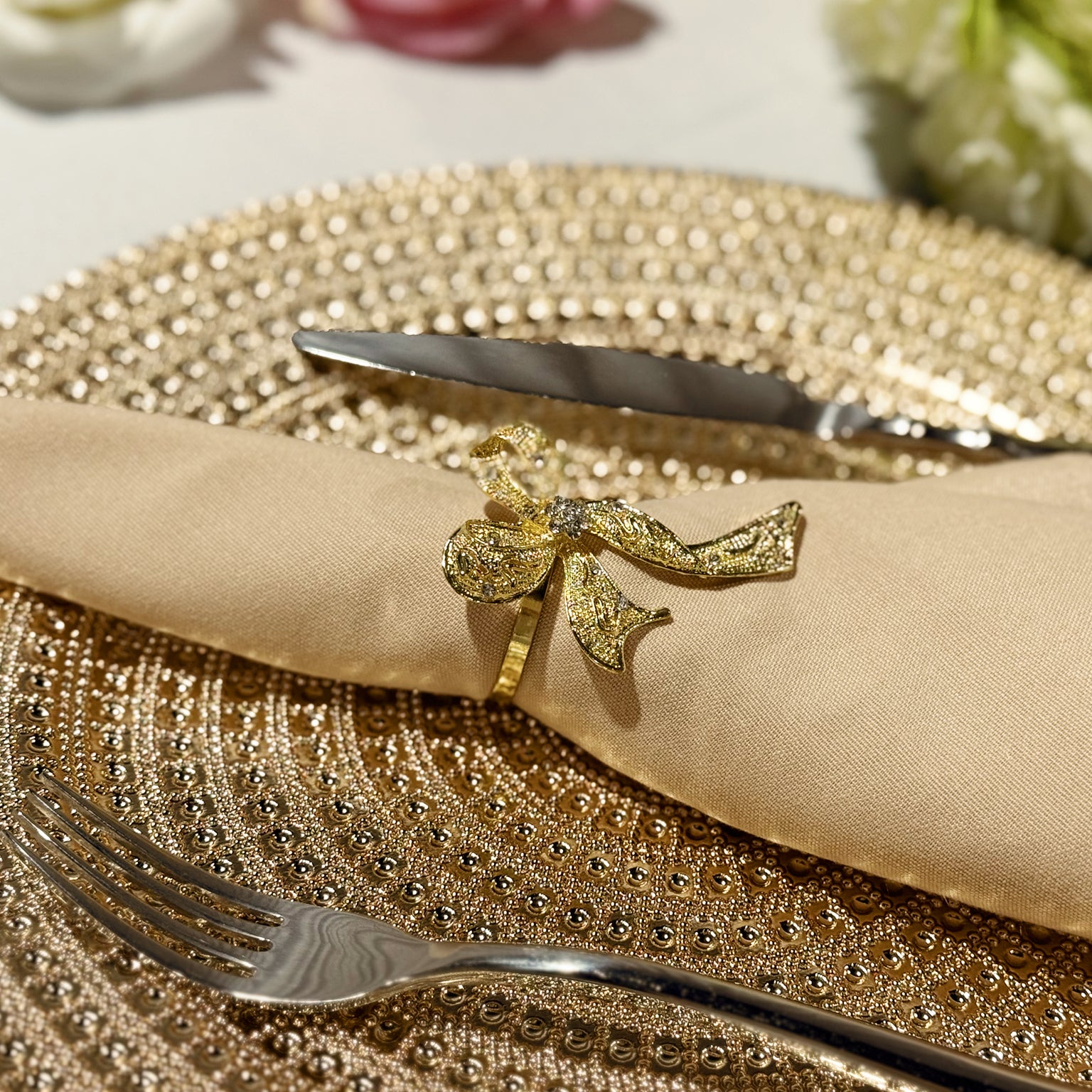 Premium Spun Polyester Napkin 20"x20" - Champagne with a gold ribbon napkin ring on top of a gold charger plate and silverware