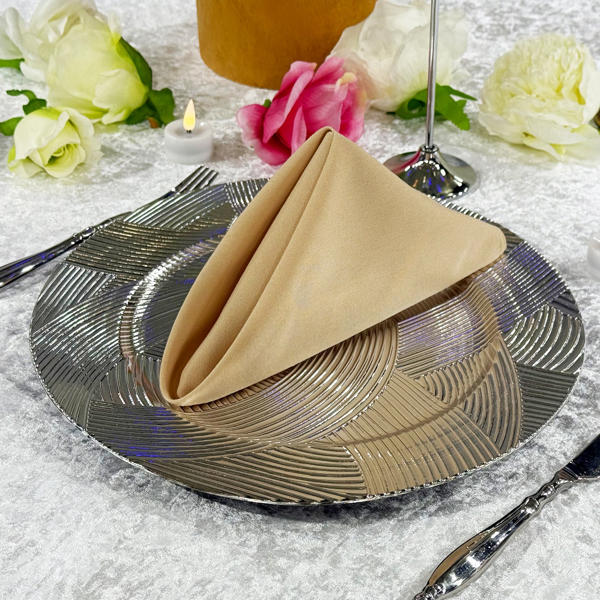Premium Spun Polyester Napkin 20"x20" Champagne folded into a triangle ontop a silver charger plate