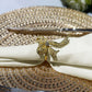 Premium Spun Polyester Napkin 20"x20" Ivory rolled with a gold bow napkin ring ontop a gold charger plate